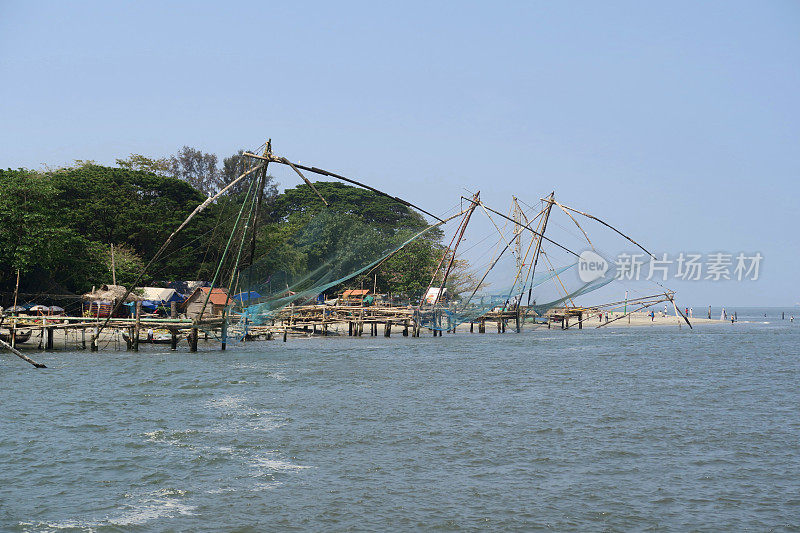 在印度南部喀拉拉邦科钦的科钦堡海滩，中国渔民在晴朗的天空下捕鱼，渔船和椰子树在阿拉伯海的科钦港水域捕捞金枪鱼和鲭鱼，Cheena vala中国渔民在科钦捕鱼